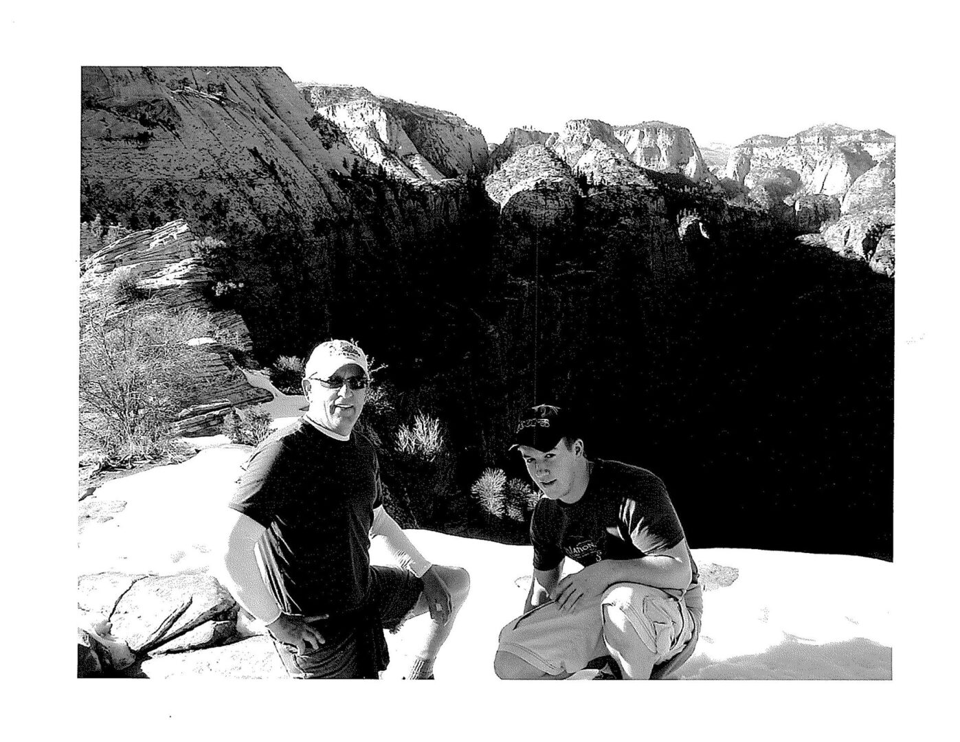 Two people sitting on the ground in front of a cave.