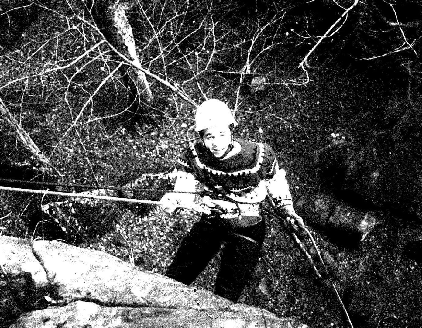 A man in black and white climbing up a tree.