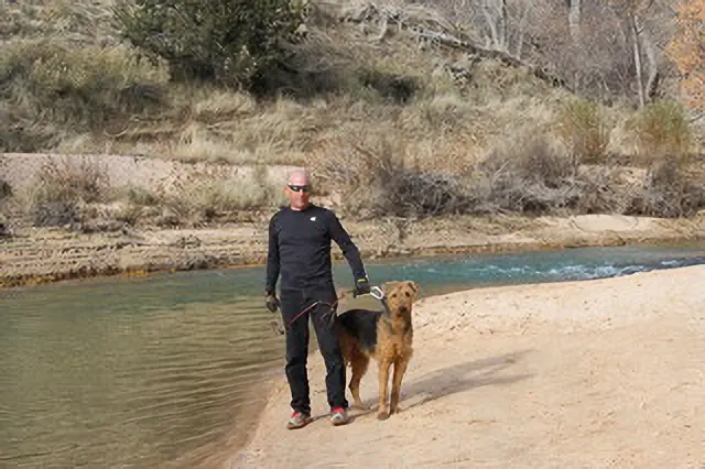 A man and his dog are standing by the water.