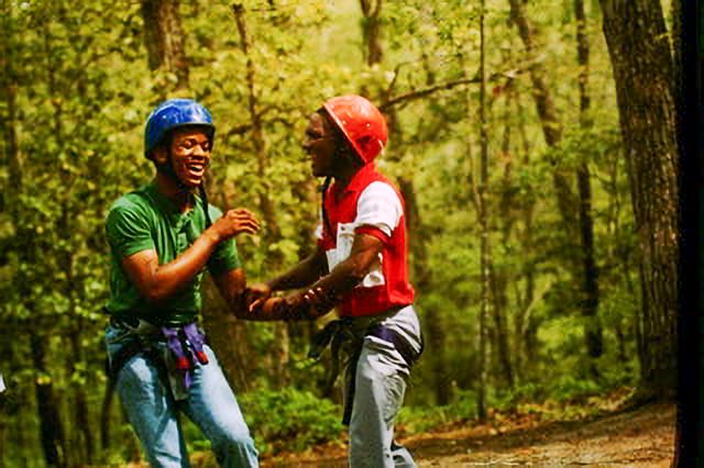 Two men laughing while wearing helmets and ropes.