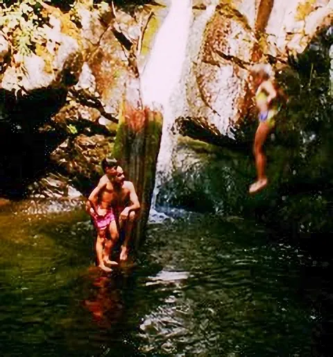 A man and woman in the water near a waterfall.